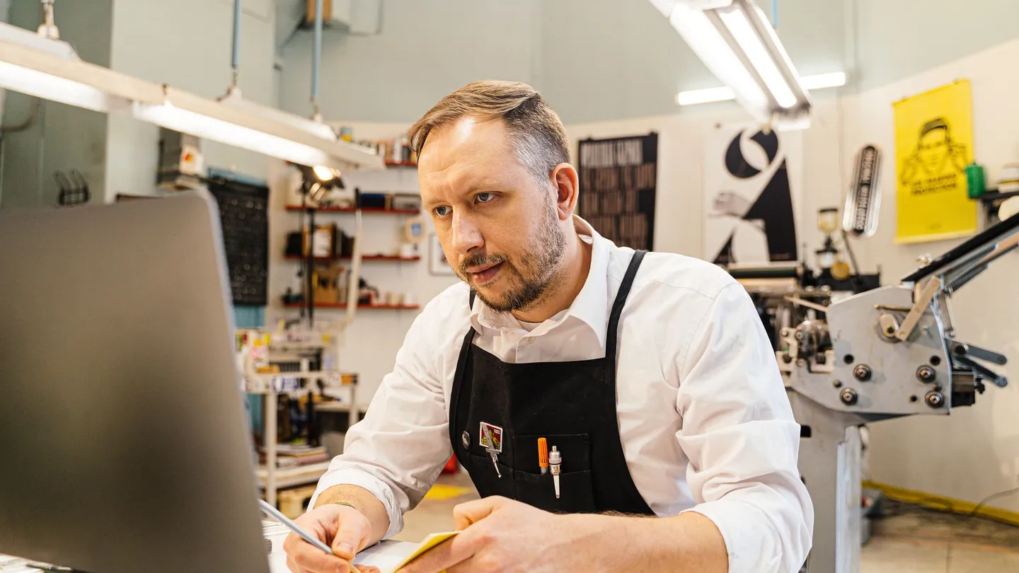 Un artisan imprimeur travaille sur son ordinateur portable au milieu de son atelier